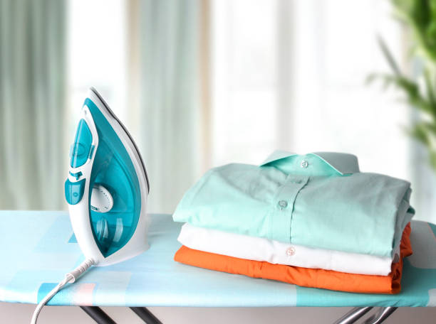 A blue iron and neatly folded shirts sit on an ironing board.
