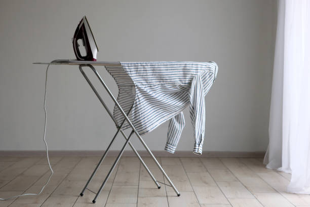 Why are ironing boards often bought but not used? 1 Striped shirt draped over a modern ironing board with an iron nearby in a room.