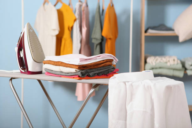 Electric iron and neatly folded laundry stacked on an ironing board.