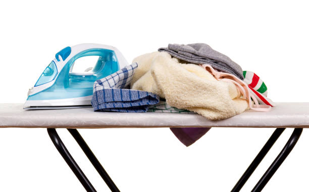Why are ironing boards often bought but not used? 2 Pile of laundry and a blue iron on a clean white ironing board.