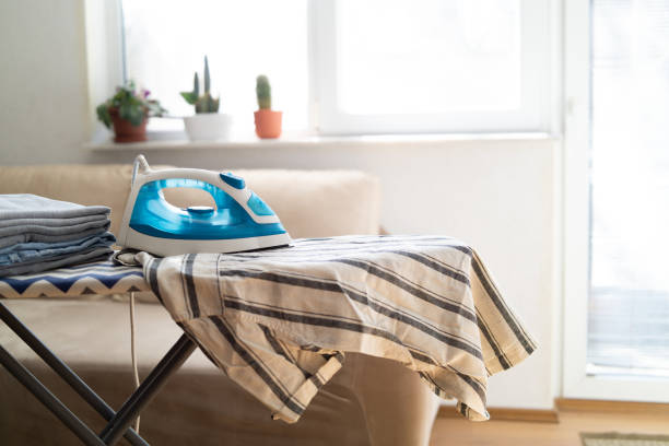 A blue iron and a striped shirt are ready for pressing on an ironing board.