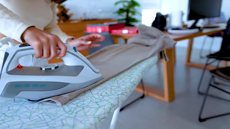 Why are ironing boards often bought but not used? 3 Person's hands ironing trousers on a patterned ironing board in a home or office.