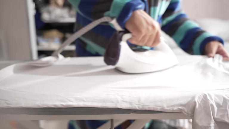 Ironing Board and the Formation of Clothing Aesthetic Standards 3 Close-up of hands ironing a white shirt on a sturdy ironing board.