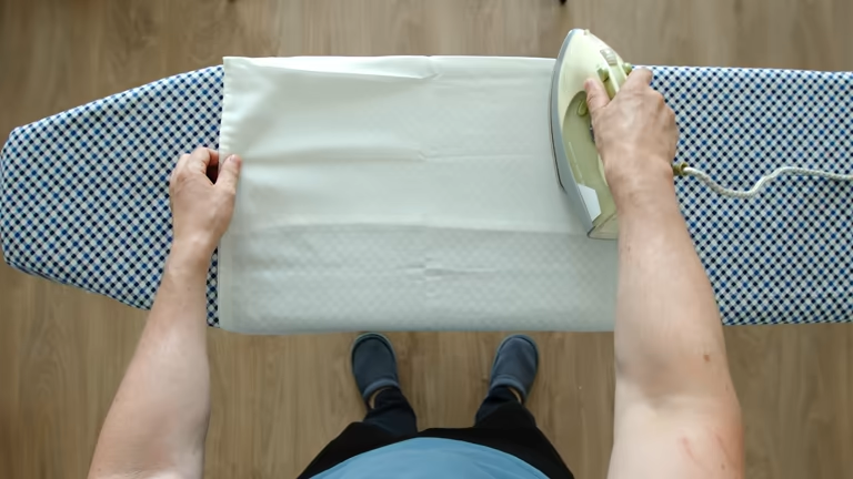 Overhead view of hands ironing white fabric on a blue checkered ironing board.