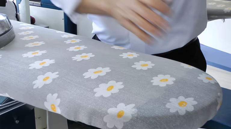 Close-up of a patterned ironing board with white daisies and a person's hands.
